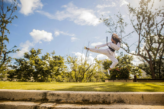 Person in white gi performing a flying kick outdoors under blue sky martial arts for fitness beginners