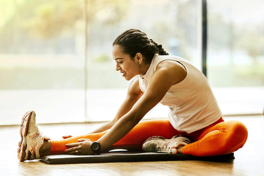 Woman performing easy flexibility exercises for beginners stretching legs on yoga mat indoors