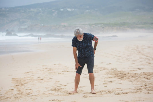 Older man on beach holding knee after workout illustrating strength training after 50 benefits for mobility