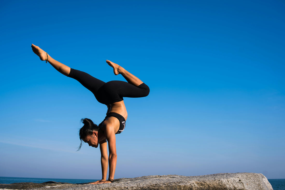 Woman performing an advanced yoga pose on a rock by the ocean, illustrating yoga for beginners step by step