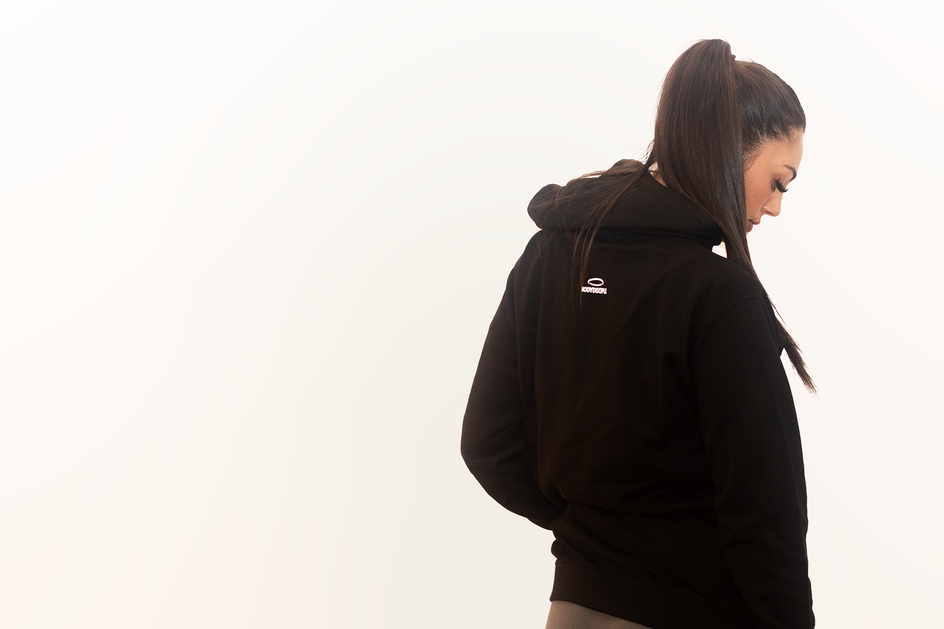 A woman, looking down, wearing Bodydisciple black hoodie B24D501BLK_Women_2